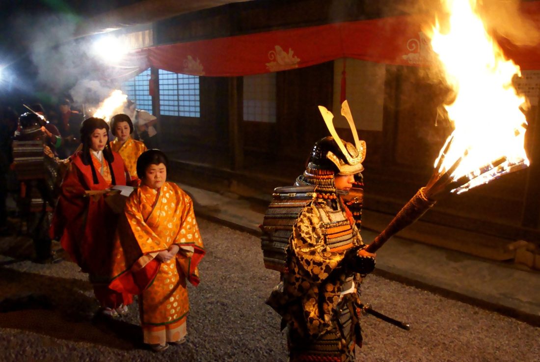 夜、松明を掲げる武者姿と十二単の女性たち