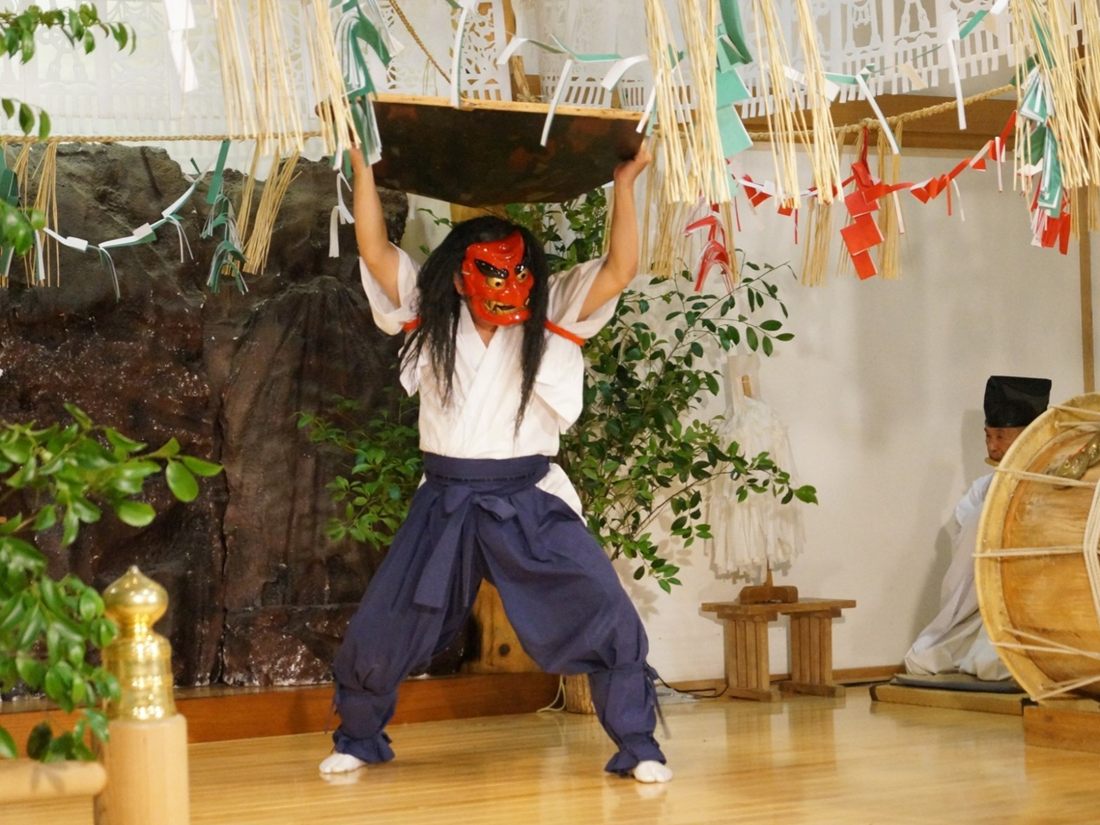 赤い面の舞い手が大きな板を頭上に掲げる神楽の場面